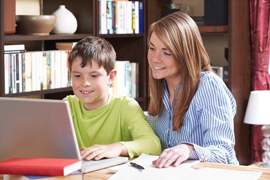 A lady tutoring a boy near a laptop at a library